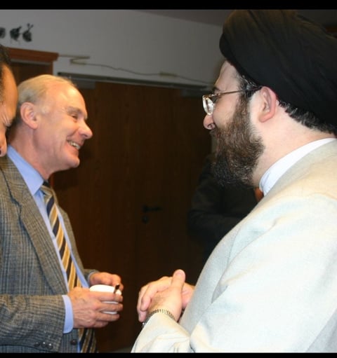Two men in professional attire shaking hands and smiling during a conversation indoors
